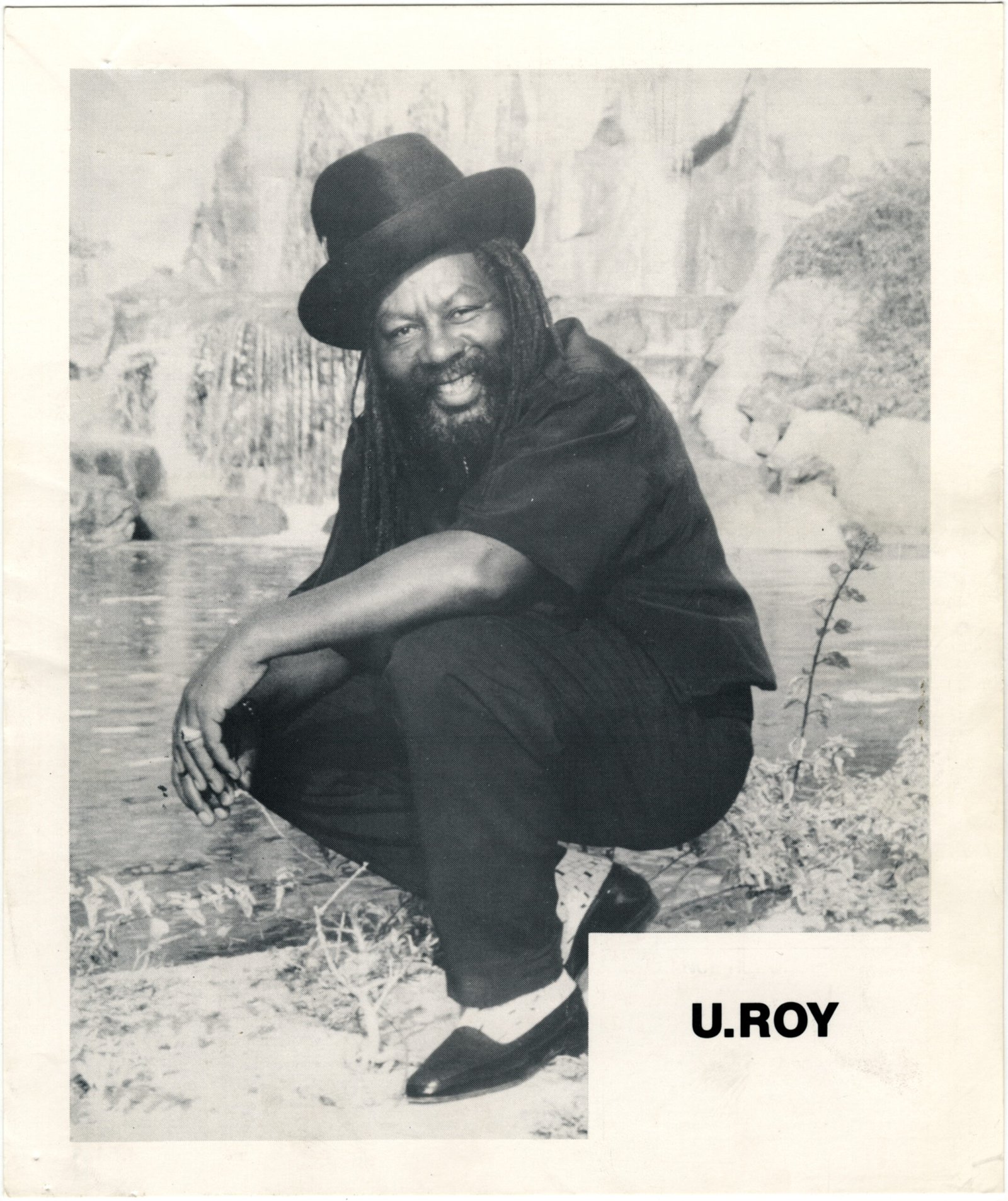 U-Roy smiling beside water in a black-and-white publicity photograph from about 1992